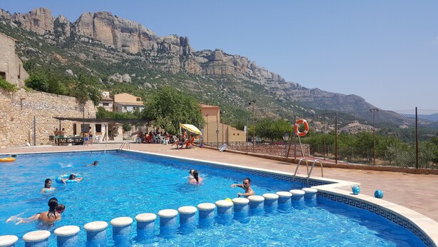 Une piscine dont le décor est constitué d’un paysage montagneux, entourée d’un mur de pierre et de quelques bâtiments.