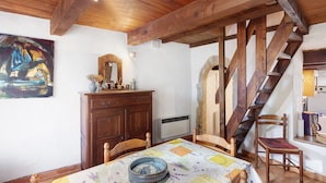 Zona pranzo con tavolo in legno, sedie, un quadro, uno specchio e una scala.