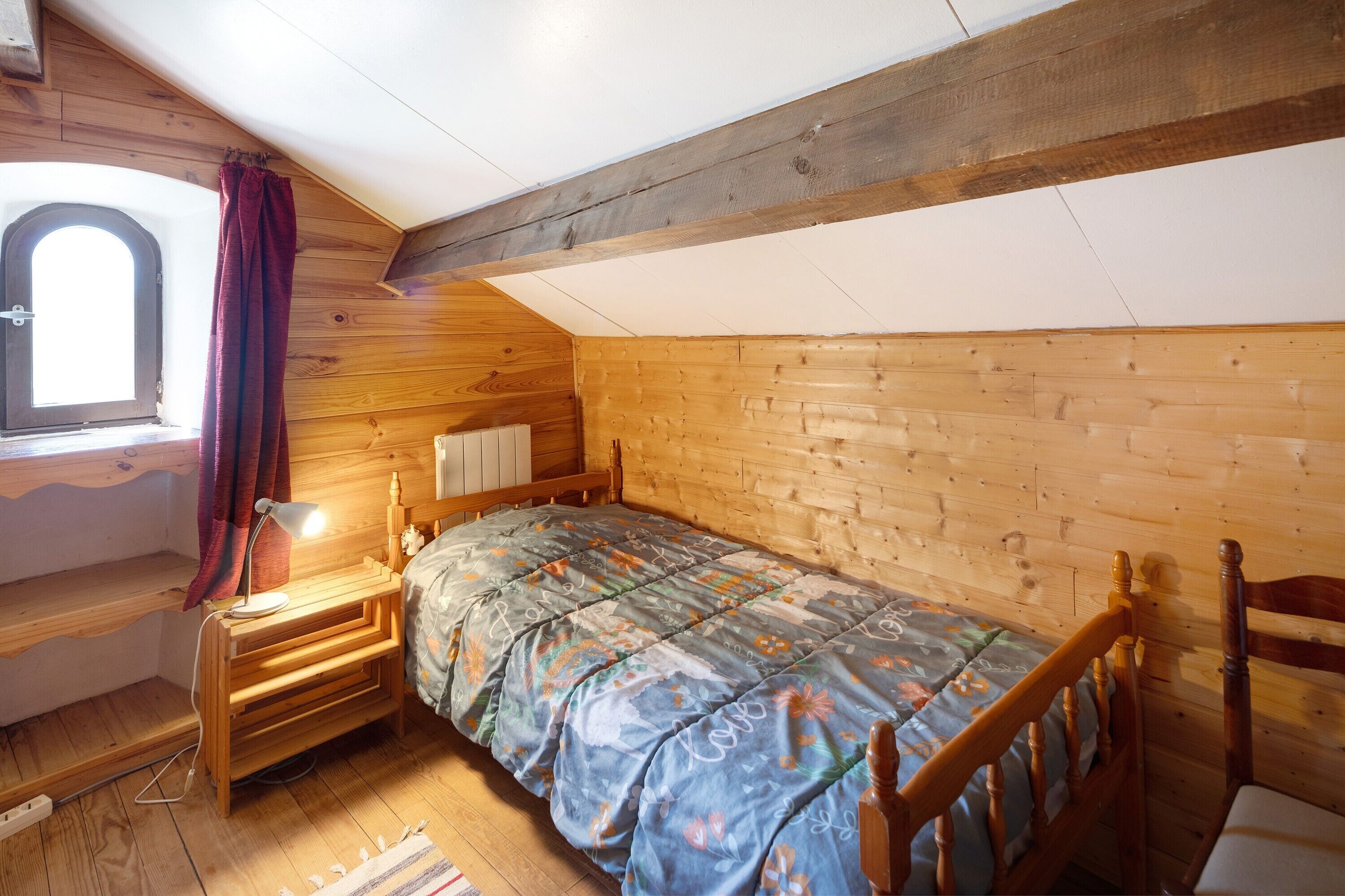 Una habitación de madera con una cama, un escritorio y una ventana con cortinas.