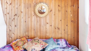 Pareti in legno con uno specchio e un letto con cuscini colorati.