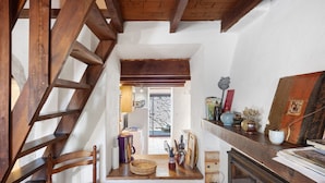 Un interno rustico con una scala in legno, un camino e uno scaffale con diversi oggetti.