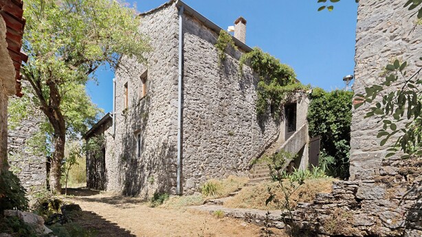 Un stretto sentiero in pietra conduce a un rustico edificio in pietra con un camino.
