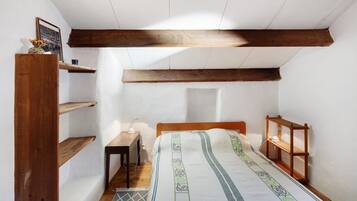 Una habitación pequeña y estrecha con una cama de madera, un escritorio y una estantería en la pared.