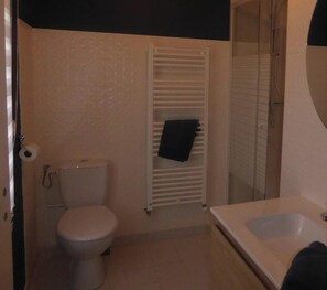 Une salle de bain comprenant des toilettes, un porte-serviettes, un espace douche et un lavabo.