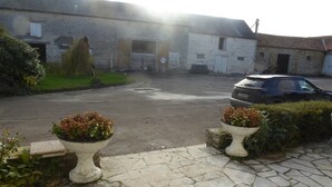 Entorno rural con un camino pavimentado que lleva a un edificio con garaje. Hay dos macetas en el pavimento.