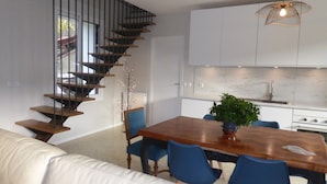 Una cocina moderna con armarios blancos, una mesa de comedor de madera, sillas azules y una escalera con escalones de madera.