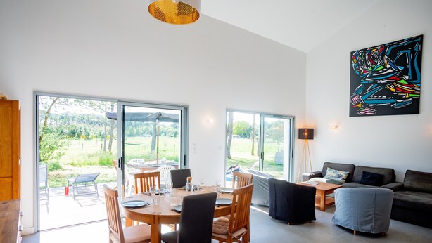 A modern living room with a dining area, large windows, and a colorful abstract painting. - Holiday Home 'Villa Surf and Golf' (MESSANGES)