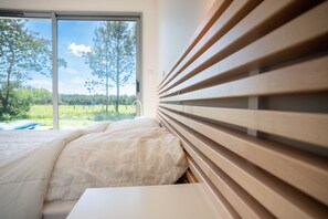 Un dormitorio con cama, ventana que ofrece vistas a árboles y cielo, y listones de madera en la pared.