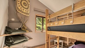 A bunk bed with a headboard, a shelf with folded towels, a hanging tapestry, and a window with a view of greenery. - Skioura Holiday Home, Group Accommodation (Bagnères-de-Luchon)