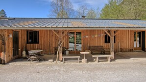 A wooden building with a metal roof, a covered outdoor seating area, and a gravel ground. - Skioura Holiday Home, Group Accommodation (Bagnères-de-Luchon)