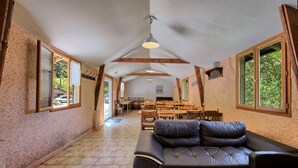 A spacious room with a large leather sofa, wooden tables, and chairs, and large windows with a view of greenery. - Skioura Holiday Home, Group Accommodation (Bagnères-de-Luchon)