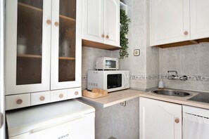 Une cuisine avec des meubles blancs, un four à micro-ondes, un évier et une planche à découper en bois.