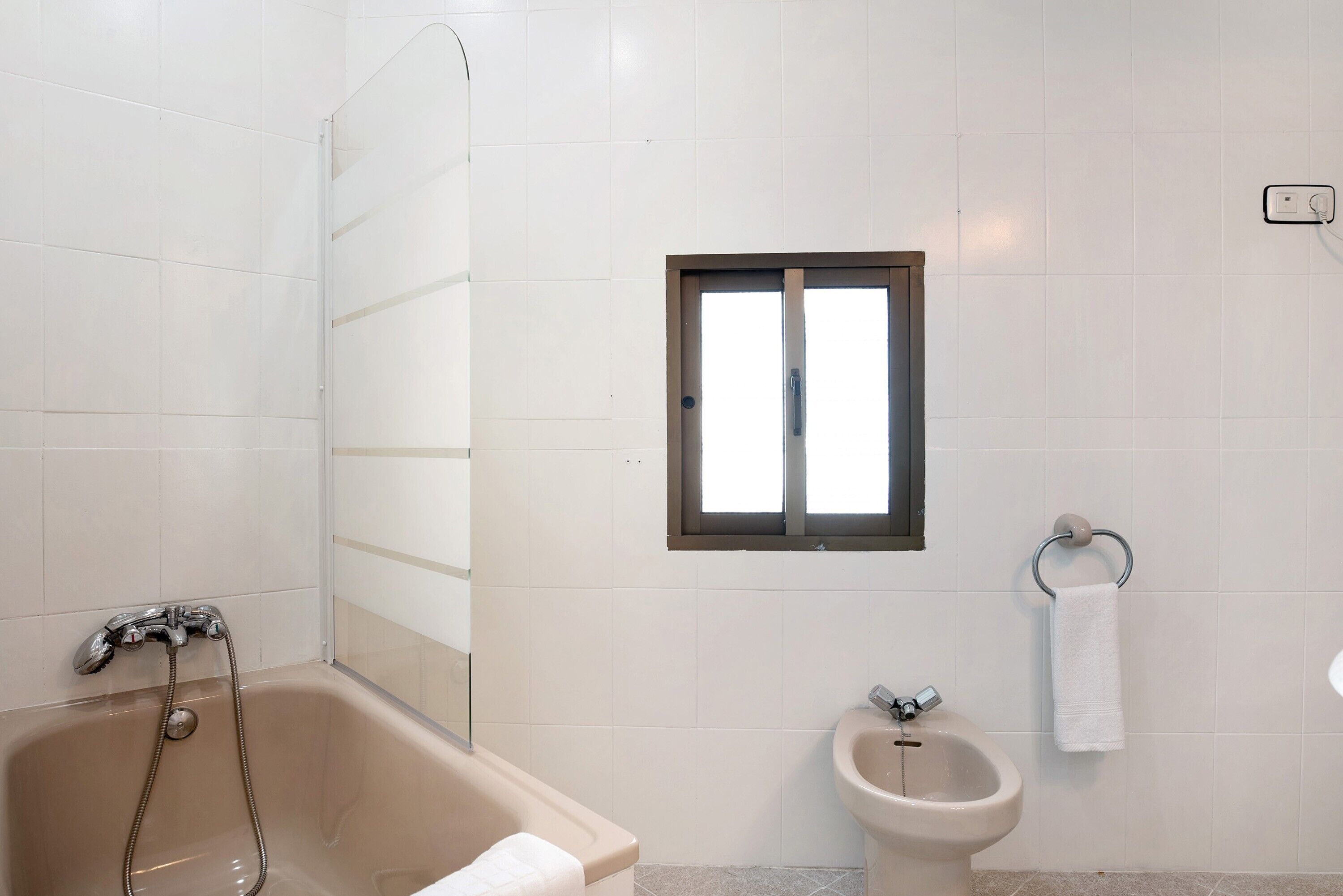 A bathroom with a bathtub, a bidet, and a window.
