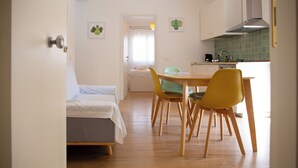 A compact room with a bed, a dining table with chairs, a kitchenette, and a door leading to another room. - Solemar Sicilia - Casa Britta  (Santa Flavia)