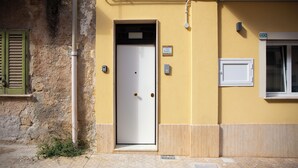 A building with a yellow exterior, a white door, and a window with a white frame. - Solemar Sicilia - Casa Britta  (Santa Flavia)