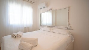 A neatly made bed with white linens and two rolled towels, a large ornate mirror above it, and an air conditioning unit on the wall. - Solemar Sicilia - Casa Britta  (Santa Flavia)