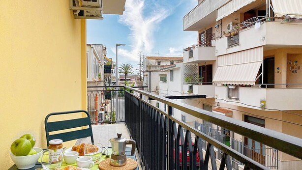 A balcony with breakfast items, a chair, and a view of adjacent buildings. - Solemar Sicilia - Casa Britta  (Santa Flavia)
