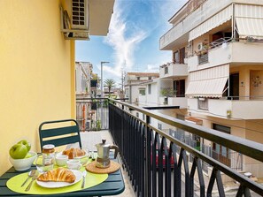 Un balcón con alimentos para el desayuno, una silla y vistas de edificios cercanos.