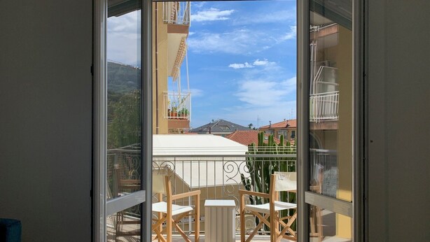 A balcony with a table and chairs, a potted plant, and a view of buildings and mountains. - Apartment 'Casa Federica' with Balcony and Wi-Fi (Alassio)