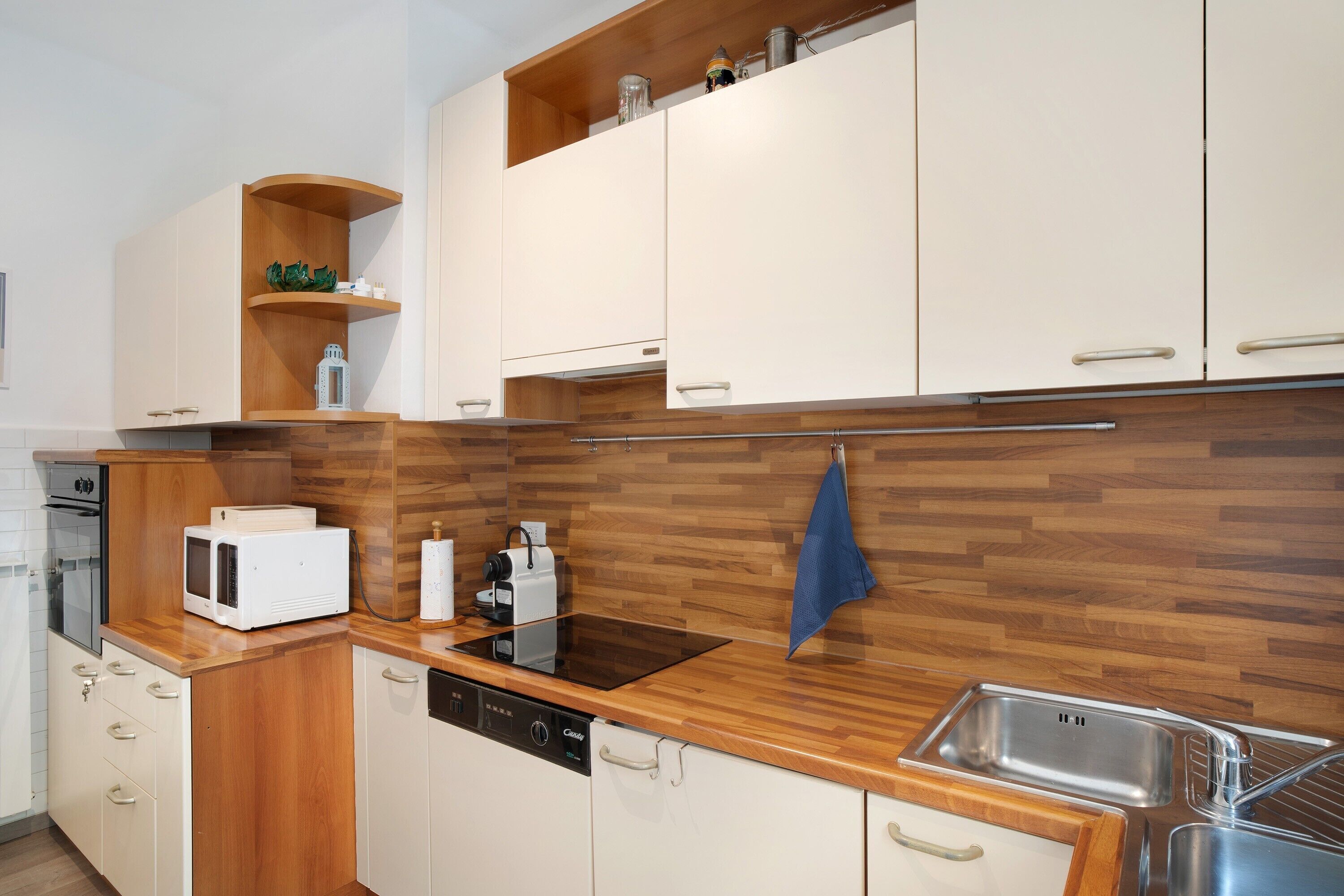 Une cuisine moderne dotée de meubles en bois, d’un four à micro-ondes encastré, d’un lave-vaisselle et d’un évier en acier inoxydable.