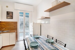 Une cuisine avec des meubles blancs, un plan de travail en bois, une table à manger avec des chaises et un réfrigérateur.