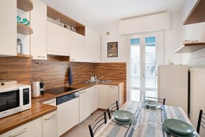 Une cuisine moderne avec des meubles blancs, des plans de travail en bois et un coin repas agrémenté d’une nappe à rayures.