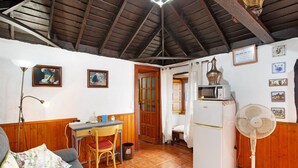Una cocina compacta con refrigerador, ventilador, mesa de madera con una silla y un sofá con cojines estampados.