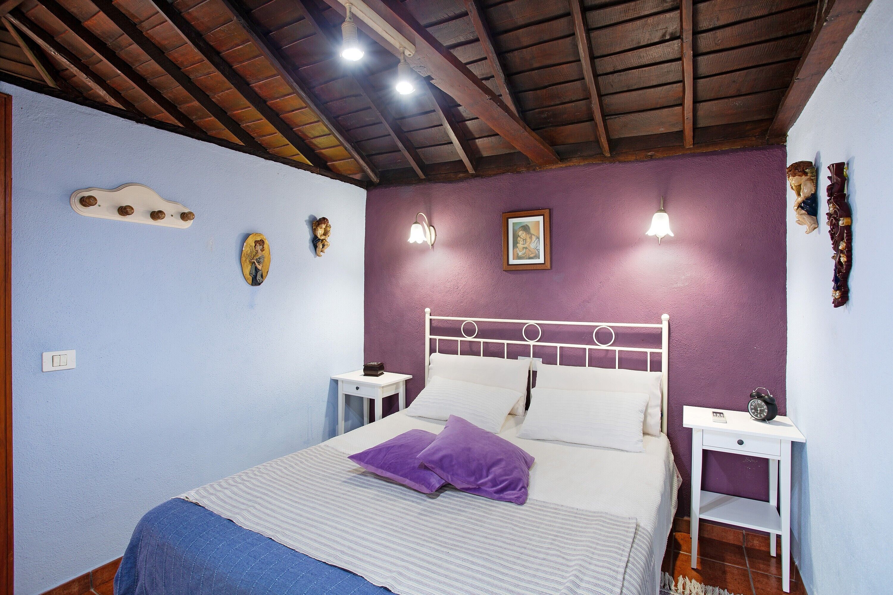 A bedroom with a bed, two bedside tables, a wall-mounted light fixture, and a ceiling fan.