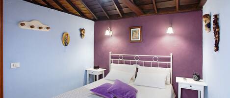 A bedroom with a bed, two bedside tables, a wall-mounted light fixture, and a ceiling fan.