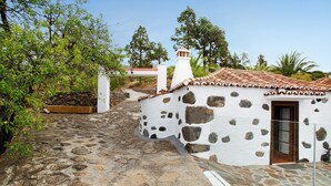 Un camino empedrado que conduce a un edificio blanco con techo de tejas, rodeado de vegetación y un muro de piedra.