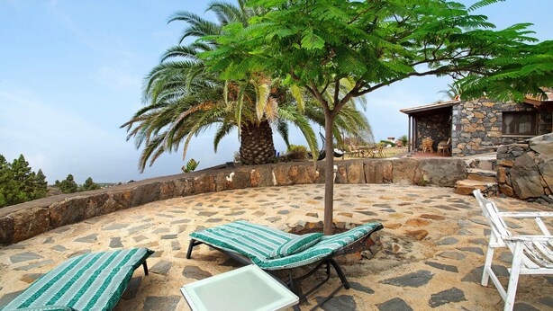 A sun lounge area with lounge chairs and a table, surrounded by a stone patio and a view of the ocean. - Holiday Home 'La Roquina' with Sea View, Wi-Fi and Air Conditioning (Tijarafe)