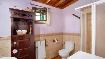 Une salle de bain avec un meuble en bois, des toilettes et un espace douche.