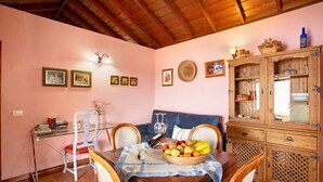 A dining area with a wooden table, chairs, a fruit basket, and a cabinet with glass doors. - Holiday Home 'La Roquina' with Sea View, Wi-Fi and Air Conditioning (Tijarafe)