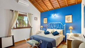 A bedroom with a bed, bedside tables, a chair, a radiator, a window with curtains, and a ceiling fan. - Holiday Home 'La Roquina' with Sea View, Wi-Fi and Air Conditioning (Tijarafe)