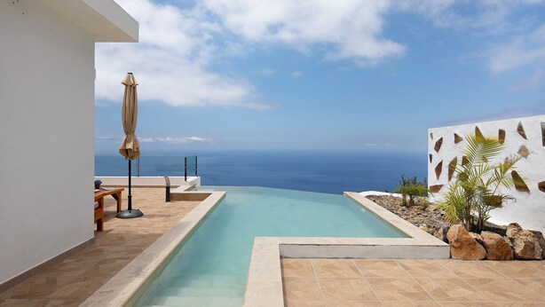 A swimming pool with a view of the ocean, a patio area with a table and chairs, and a wall with decorative elements. - Holiday Home 'Valista' with Sea View, Private Pool and Wi-Fi (Tijarafe)