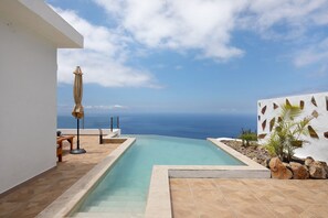 A swimming pool with a view of the ocean, a patio area with a table and chairs, and a wall with decorative elements. - Holiday Home 'Valista' with Sea View, Private Pool and Wi-Fi (Tijarafe)