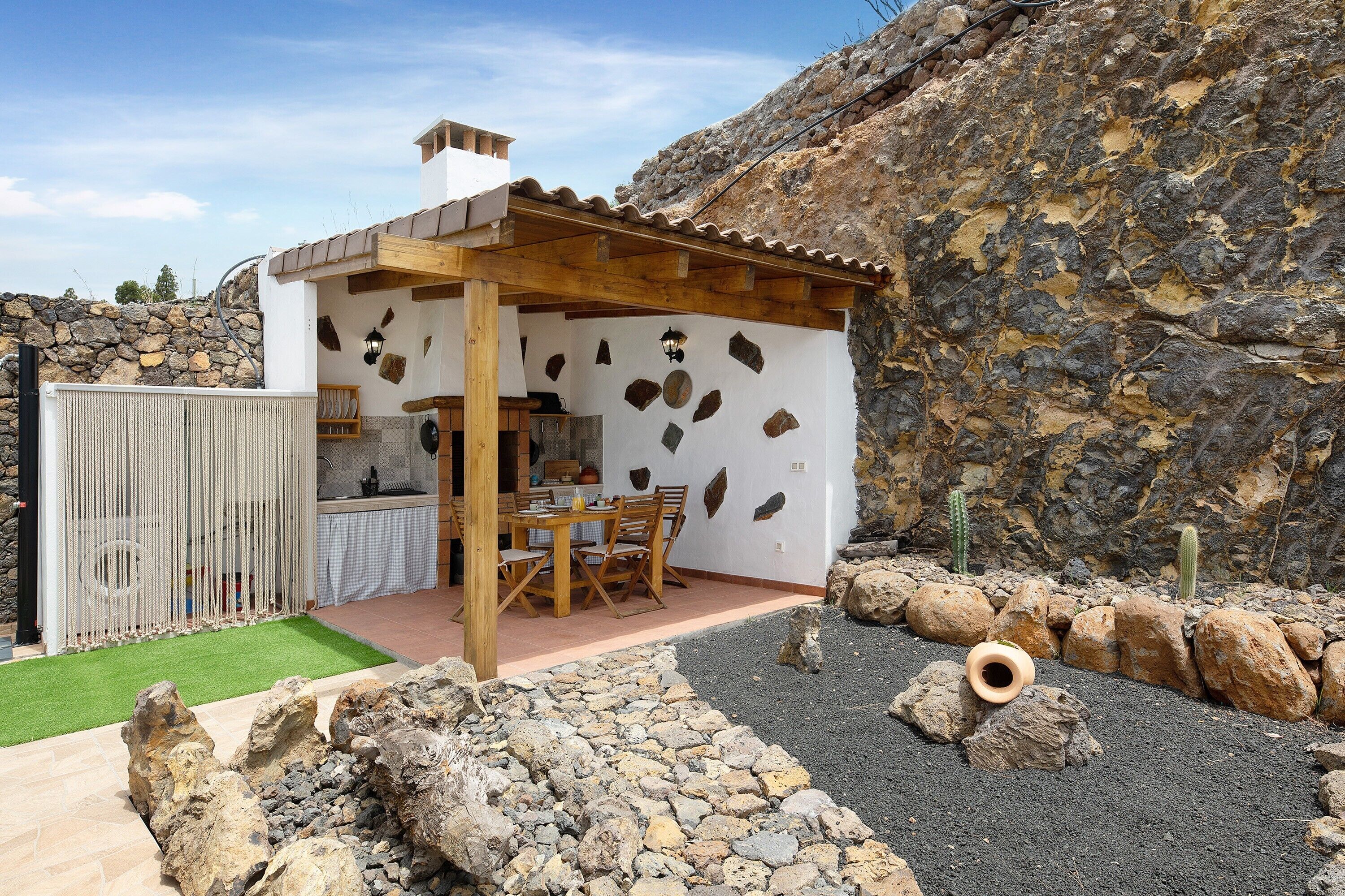 Et stenhus med en træpergola, et spiseområde og en klippehave.