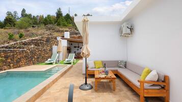 Un espace aménagé au bord de la piscine, avec un mur en pierre, des chaises longues, un canapé et une table sur laquelle se trouvent une bouteille et des verres.
