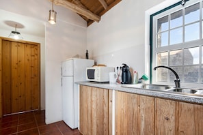 Una cocina con armarios de madera, microondas, hervidor y ventana con vistas.