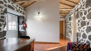 Una habitación con pared de piedra, vigas de madera en el techo, una puerta blanca y un extintor.