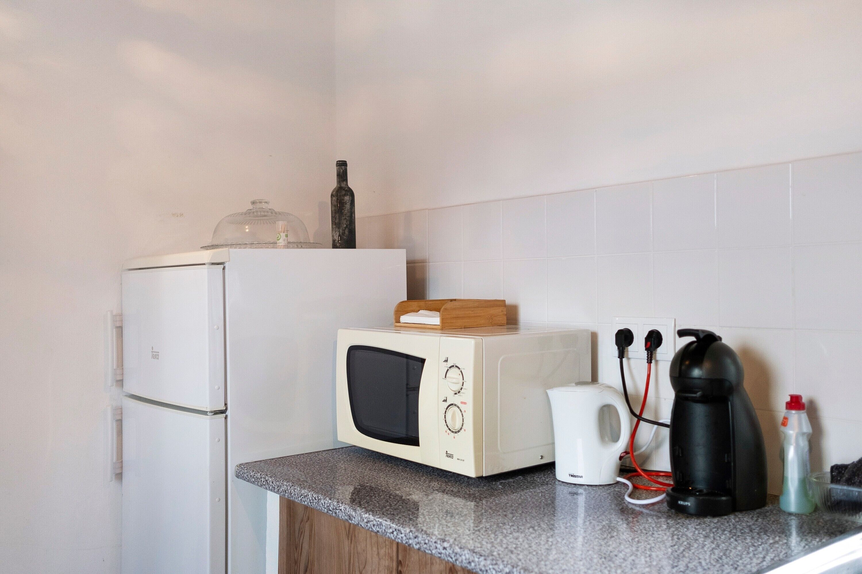 A kitchen with a white refrigerator, a microwave, a coffee maker, and a bottle on the counter.