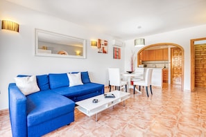 A living room with a blue sofa, white coffee table, and a dining area with chairs and a table.