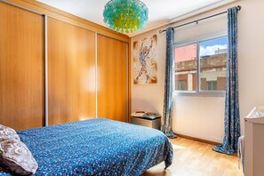 A bedroom with a bed, a wardrobe, a small table, a radiator, and a window with curtains. - Apartment 'San Antonio' with Private Terrace, Wi-Fi and Air Conditioning (Sedaví)
