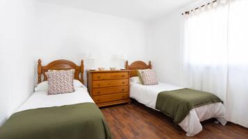 A bedroom with two single beds, a wooden dresser, and a window with curtains.