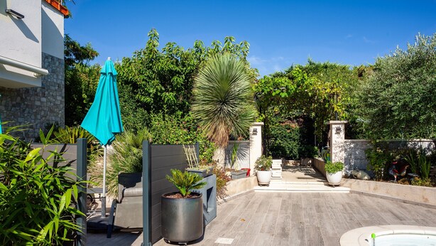 Ein Poolbereich mit Holzterrasse, blauem Sonnenschirm und Pflanzen in Töpfen.