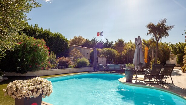 A swimming pool with a flag, surrounded by greenery and outdoor furniture. - Apartment 'Lucerta Bella' with Shared Pool, Wi-Fi and Air Conditioning (Aix-en-Provence)