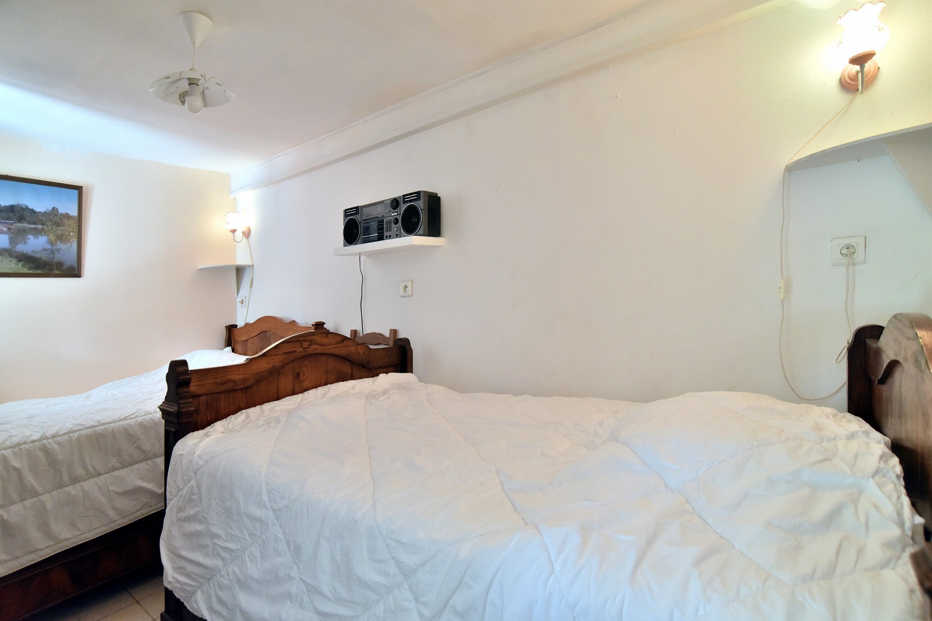 Een slaapkamer met twee eenpersoonsbedden, een plafondventilator, een radio op de muur en een bedlampje.