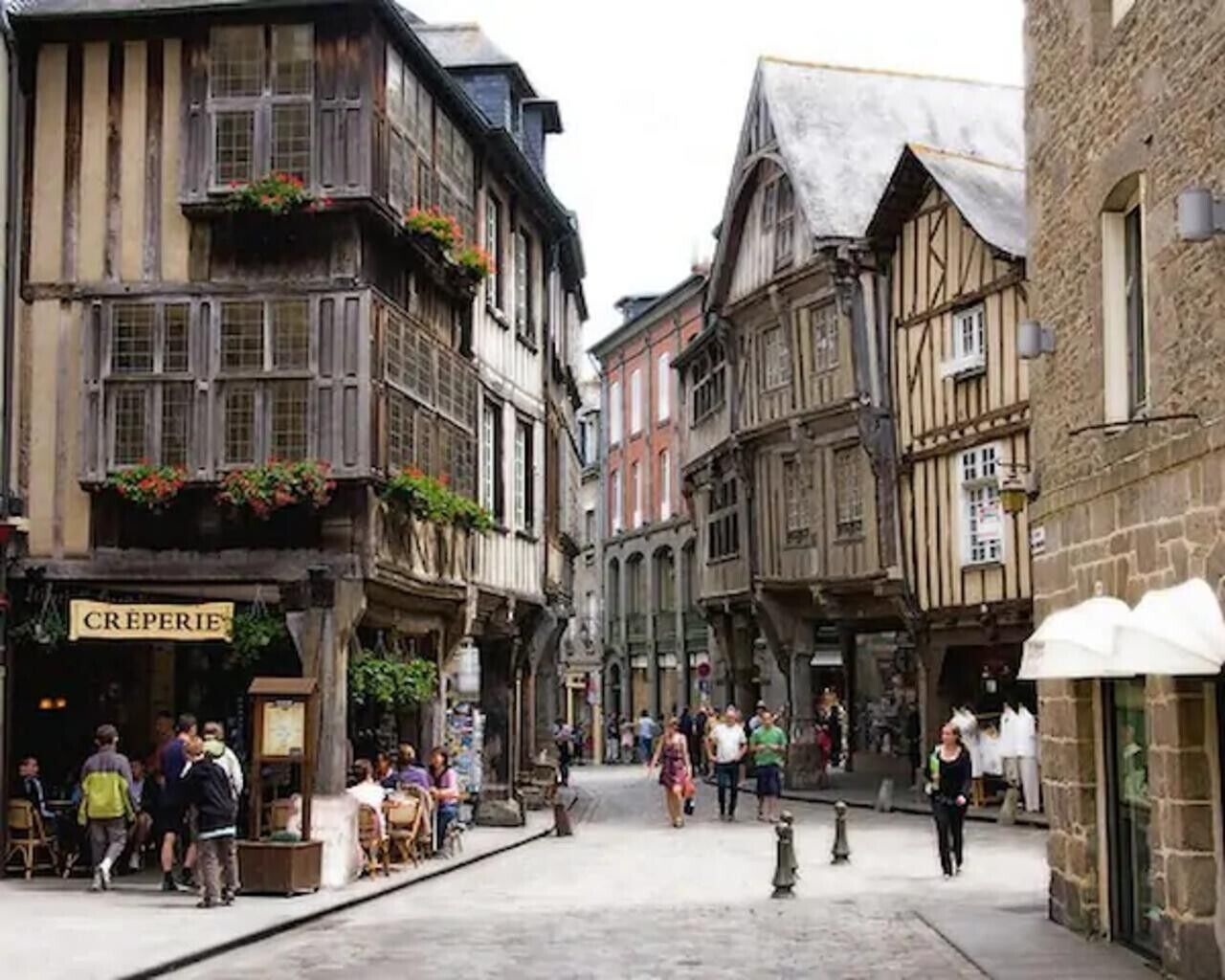 Une rue étroite bordée de bâtiments traditionnels à colombages, un café appelé « CRÊPERIE » et des piétons.