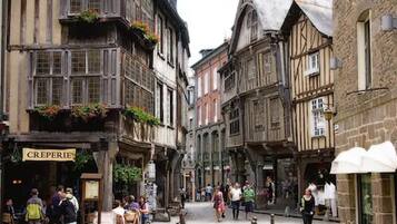 Une rue étroite bordée de bâtiments traditionnels à colombages, un café appelé « CRÊPERIE » et des piétons.