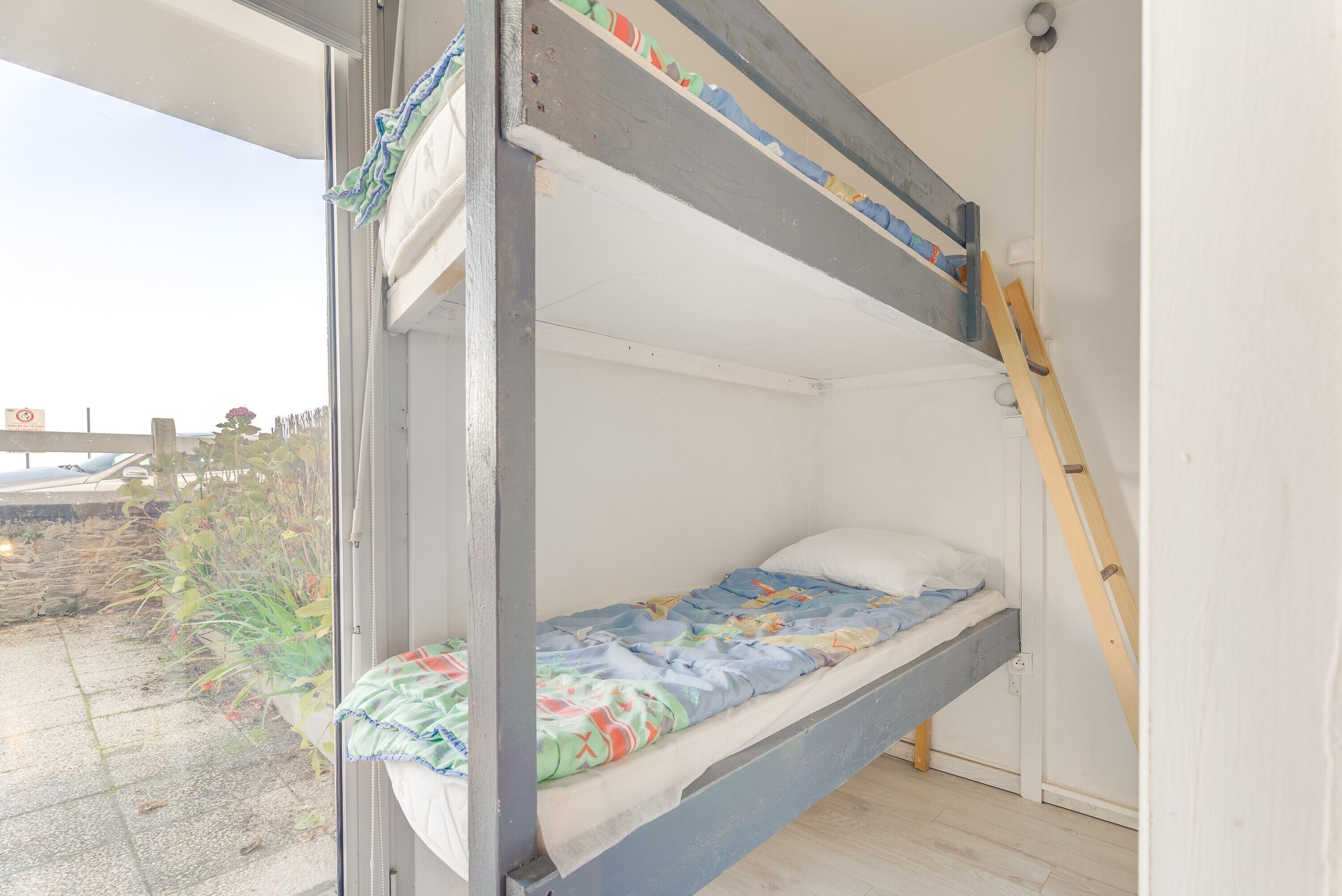 A bunk bed with a lower bunk, a ladder, and a window with a view of the outside.